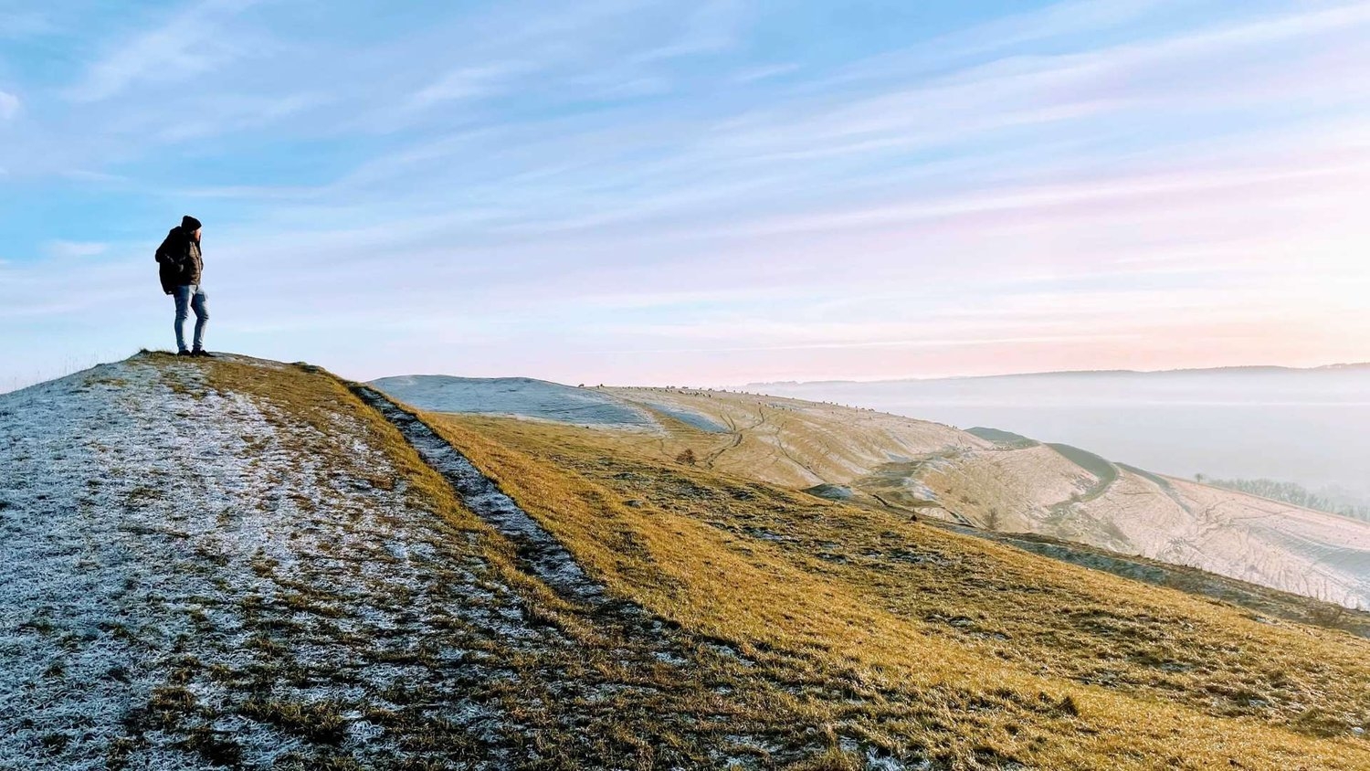 One male traveler standing on the top of Hambledon Hill admiring the blue and pink skies