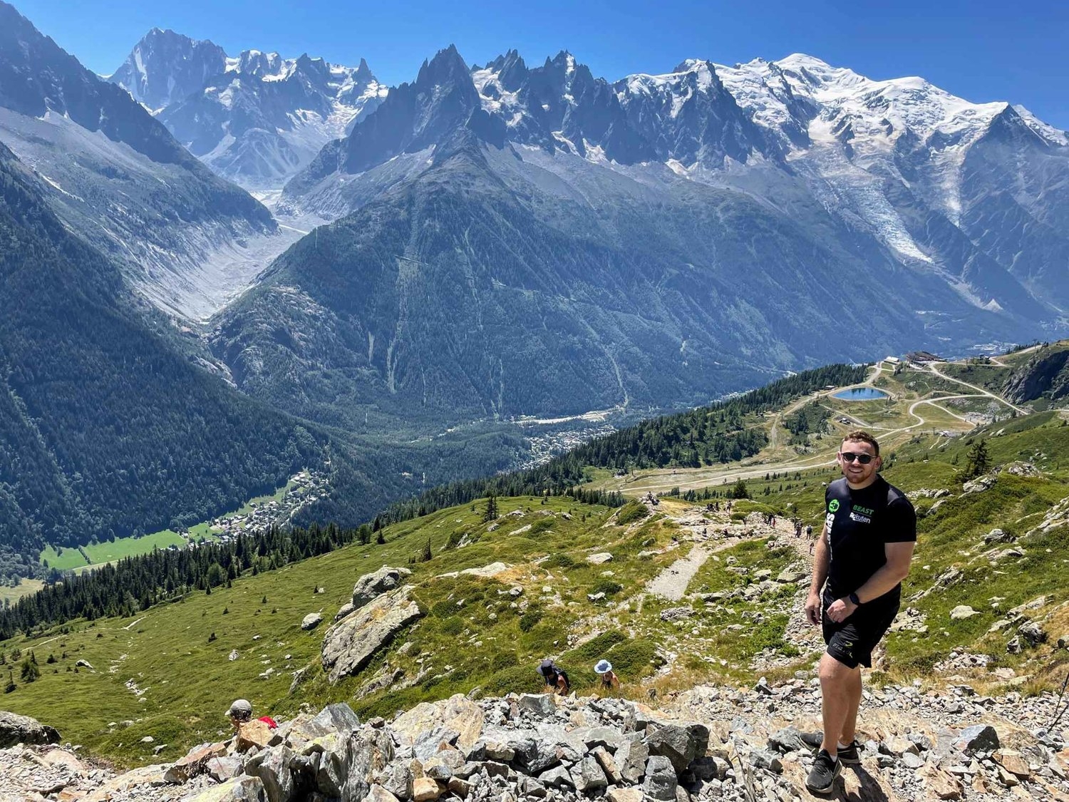 Male hiker standing on Lac Blanc trail path, standing in front of rugged mountain range and snow-capped Mont Blanc.