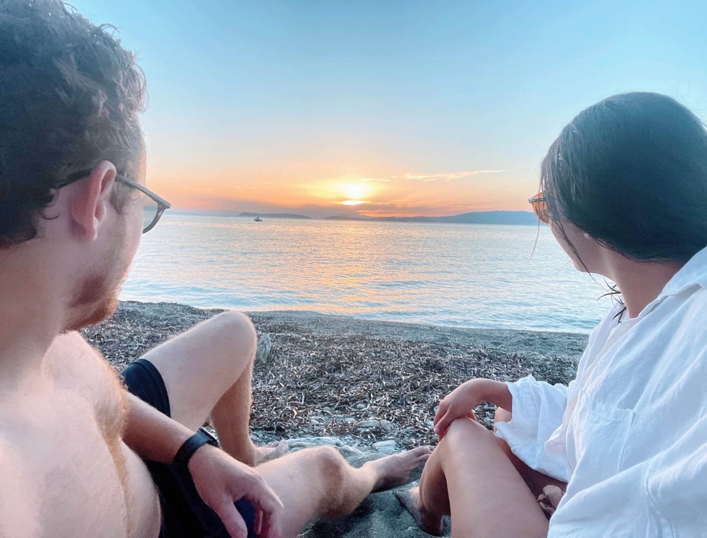 Two travellers sitting on the beach watching the sunset in Greece