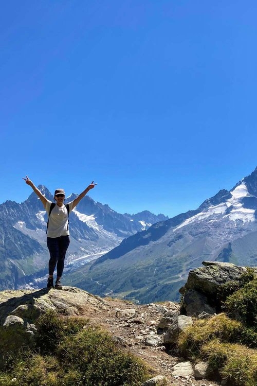 female hiker standing on top of boulder on easy lac blanc hike route in front of mont blanc mountain range