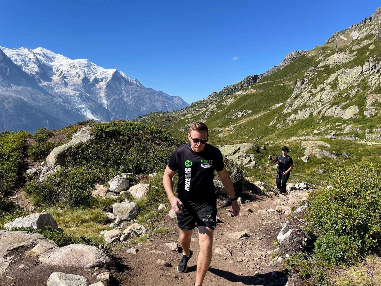 Andrew walking on Lac Blanc hike trail from L'Index to Lac Blanc with snow-capped Mont Blanc mountains behind him.